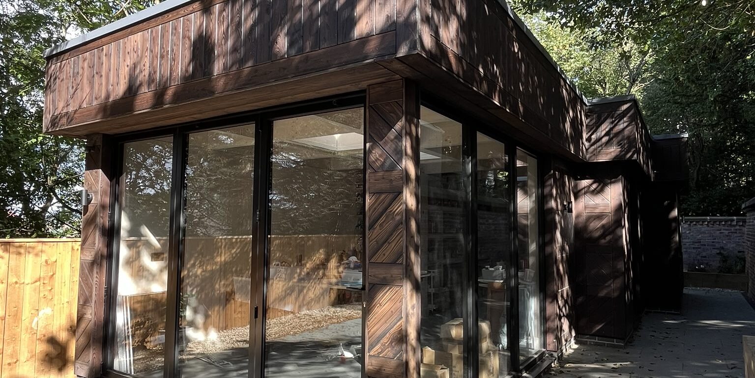 Timber-clad garden room with full-height glazing in a tree-lined garden