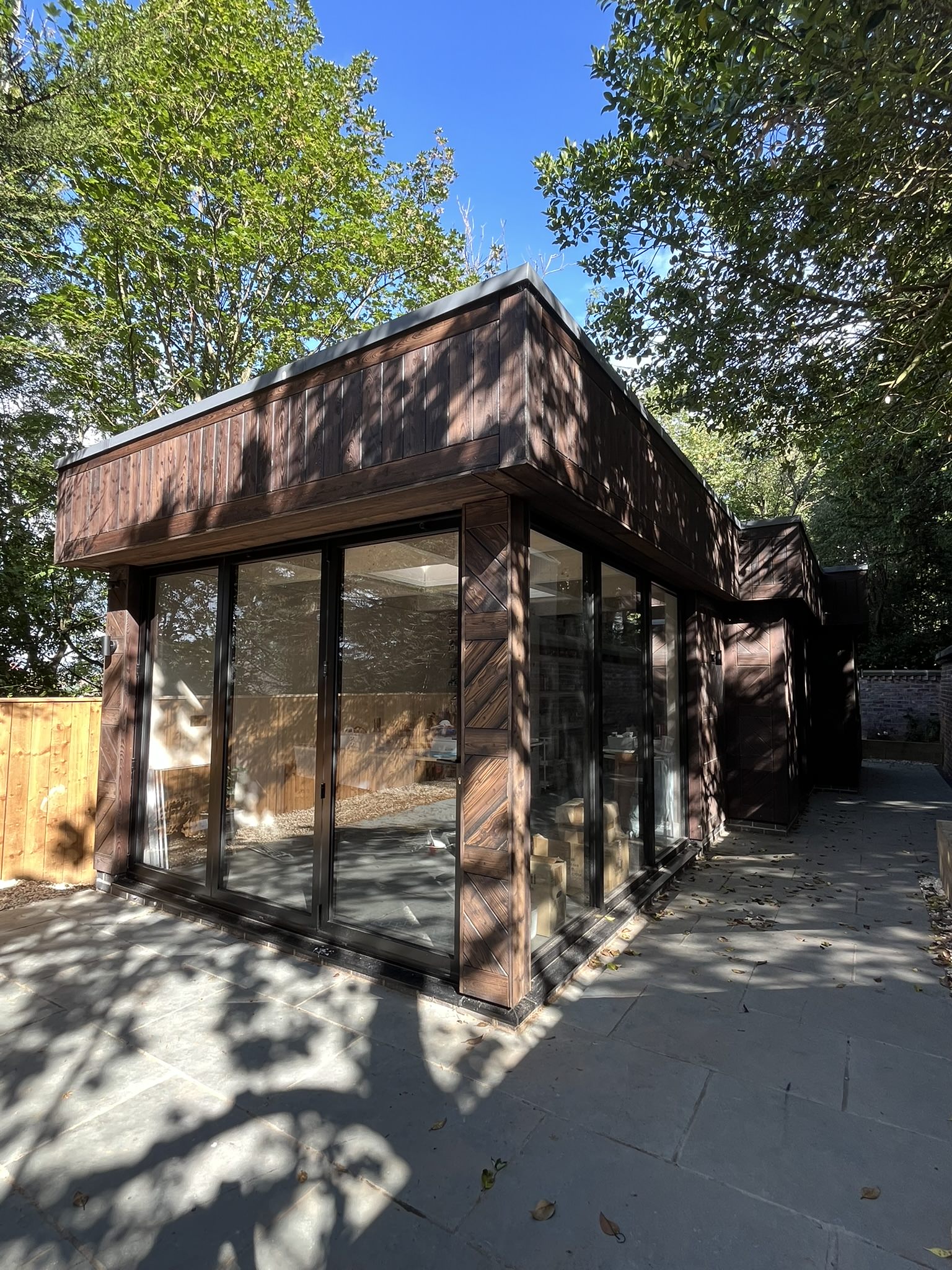 Timber-clad garden room with full-height glazing in a tree-lined garden