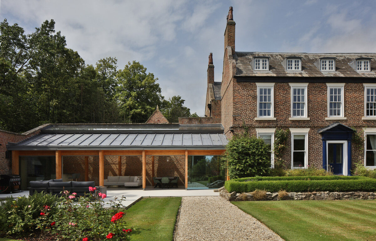 Glazed timber-framed garden pavilion beside a Georgian brick house and rose beds