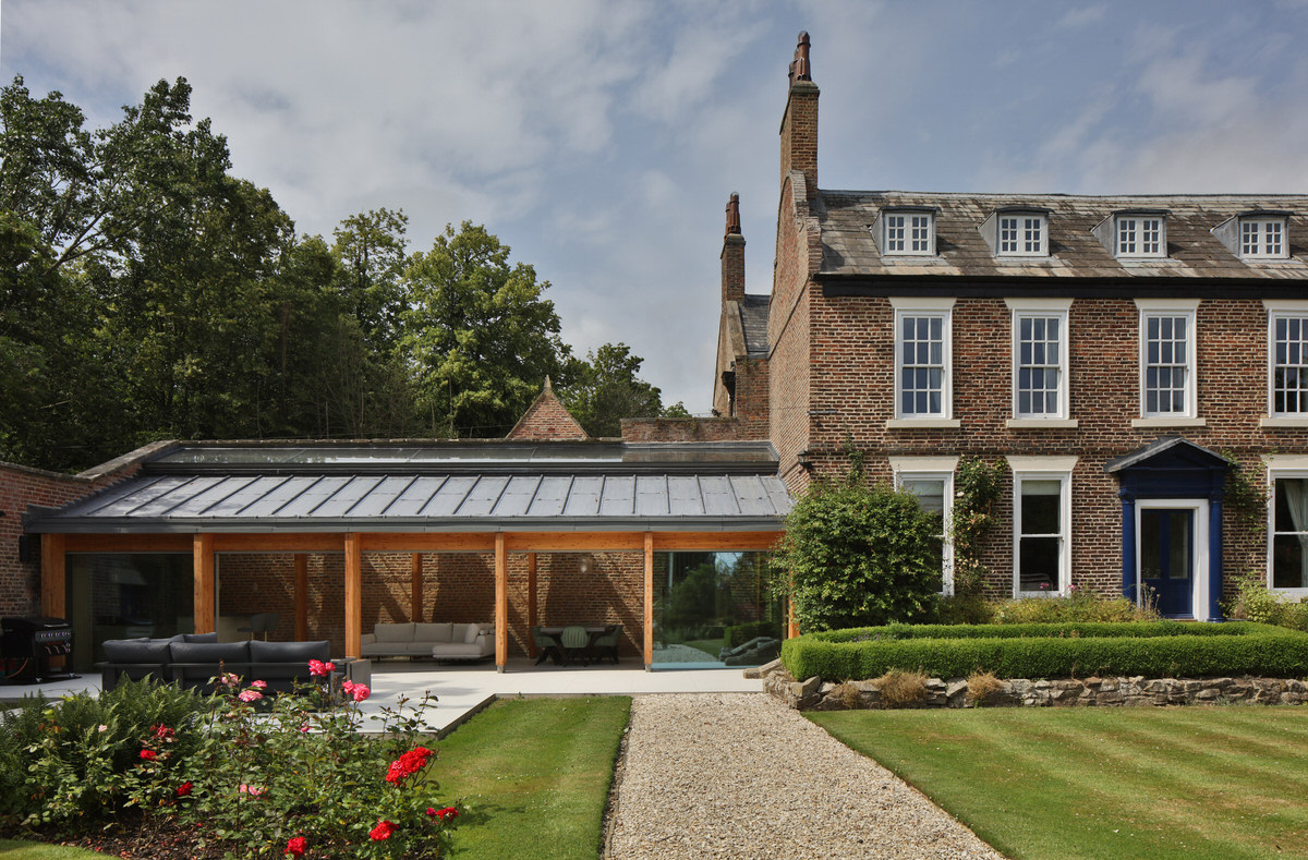Glazed timber-framed garden pavilion beside a Georgian brick house and rose beds